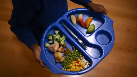 A child's school dinner tray, showing potatoes, vegetables and fruit