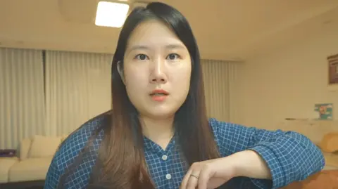 A woman, wearing a blue shirt, stares at the camera. 