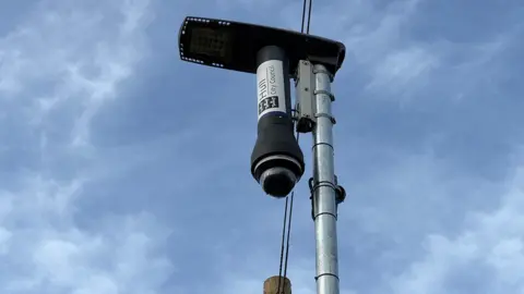 Becki Bowden / BBC One of the CCTV cameras mounted on a steel post. It has a 360 glass lenses mounted in a black T-shaped structure