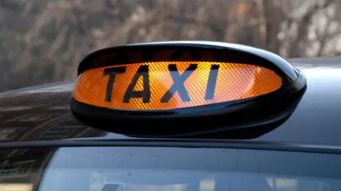 An orange 'Taxi' sign on top of a cab.