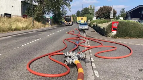 Orange fire hoses on a street with a car and lorry further down the road in the distance