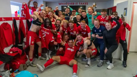 Worthing FC players in their red kit celebrate in the changing room