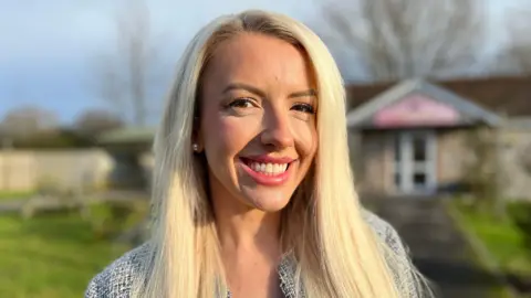 Grace Harvey standing outside the Pigs & Prosecco building at Puxton Park. She has long blonde hair and smiles at the camera.