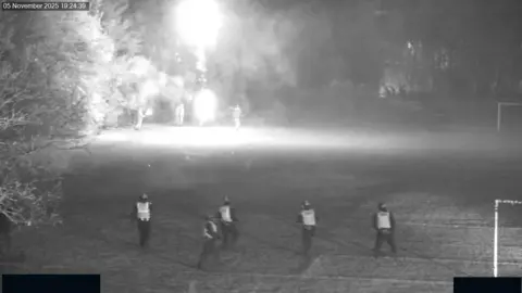 Police Scotland Black and white CCTV footage of five police officers facing youths with fireworks across a football field 