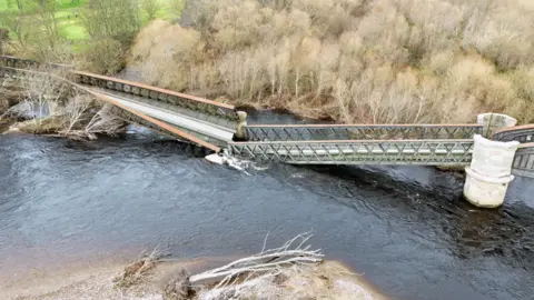 Trev Moore A collapsed iron girder bridge with a section between two stone piers breaking apart and falling into the water