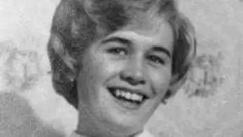 A black and white photo of a woman smiling into the camera with short, curly hair.
