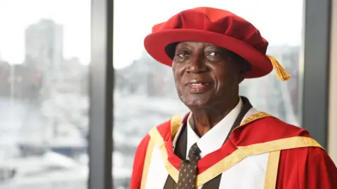 Gregg Brown/University of Suffolk A man in formal red university robes and hat