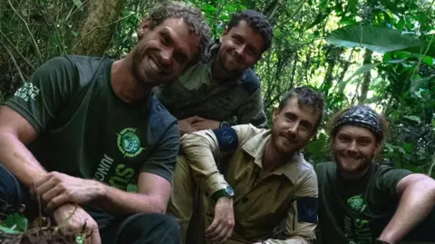 Ash Dykes Ash Dykes with team members Dick Lock, Matt Wallace and Jacob Hudson crouching down and smiling in the jungle.