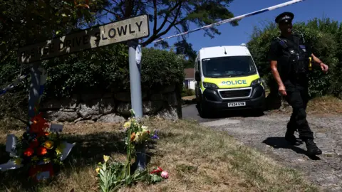 Reuters Flowers are pictured on the ground with a police officer walking down a driveway beside