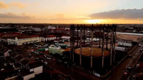 Shaun Whitmore/BBC A sunset over Great Yarmouth, over the gasometer. Its latticework and columns clearly seen in silhouette detail, with other industrial infrastructure and buildings including former smokehouses to the left of the image, and silos on the bank of the river port.