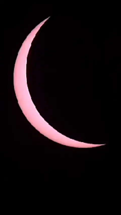 Partial solar eclipse in 2015 - a pink crescent Sun peaks from behind the Moon