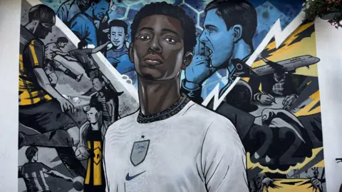 BBC/Chloe Hughes A mural of Jude Bellingham in a white England shirt, with blue and yellow football drawings behind him