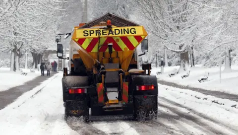 A council gritter spreads grit on snowy winter roads.