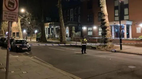 Police officer standing behind a police cordon on Friar Gate in Derby at night on Saturday 28 March 2026.