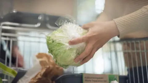 Person holds a head of lettuce wrapped in plastic