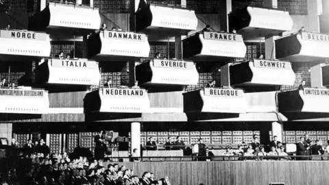 Southbank Centre A black and white photo of the inside the Royal Festival Hall with different countries' names printed on the balconies above where an audience is sitting.