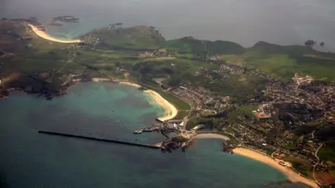 A small island with sandy beaches, fields and a small town from above.
