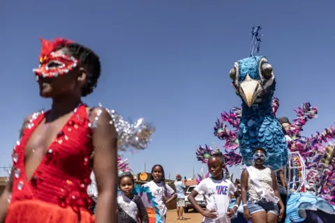 ROBERTA CIUCCIO/AFP People parade in bejewelled masks and large bird effigies.