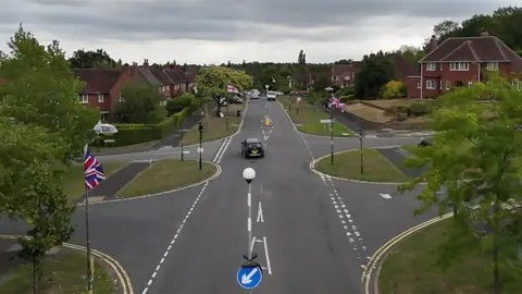 Union Jack and St George flags hang from every lamppost on a street in Birmingham, seen from an aerial drone shot.