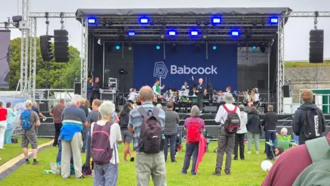 A small crowd gathers around a stage, which has the words Babcock written behind it.