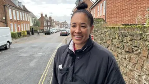 A woman in a black jacket. Her hair is tied up in a bun. 