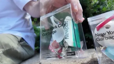 A plastic spoon and other trash in a plastic transparent cube.