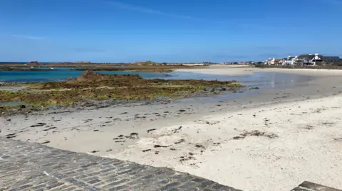 The picture shows Cobo beach on Guernsey's west coast on a sunny day with a blue sky