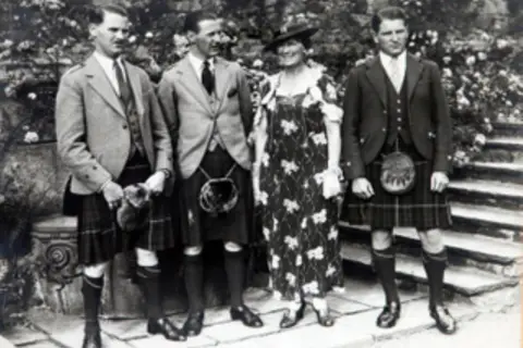 MacRobert Trust Black and white photo of three men in kilts, either side of their mother who is wearing a floral dress.