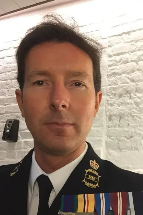 Terry Stewart A clean shaven man with short brown hair and dark eyes looks at the camera. He wears a Royal Navy blazer, white shirt and dark tie. On his chest are six medals hung on colourful ribbons. 