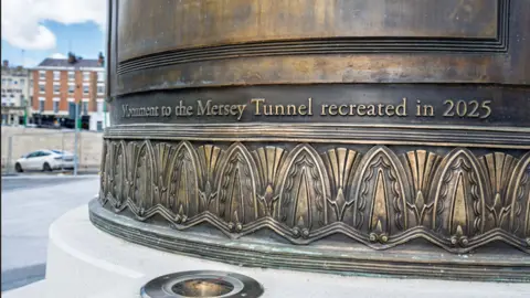 Image shows a reinforced concrete cylindrical monument on a plinth. It has been highly polished to resemble the original granite. Visible are the words "Monument to the Mersey tunnel recreated in 2025". 