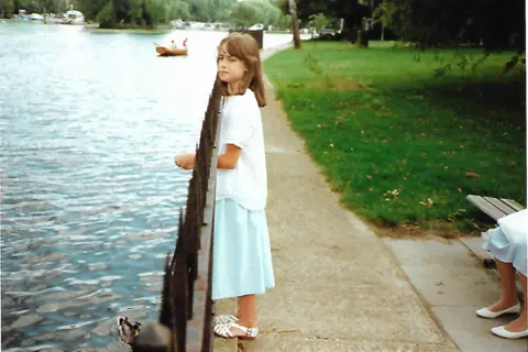 Philippa Barnes as a young girl standing at a railing in a park looking out over a lake