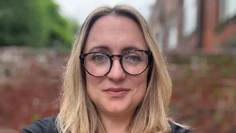 Rachael Walker, of data analytics company Policy in Practice, wearing shell-rimmed glasses. She has blonde hair and is looking at the camera.