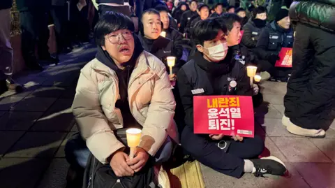 BBC / TESSA WONG Protesters hold candles and placards at a rally calling for Yoon Suk Yeol to step down