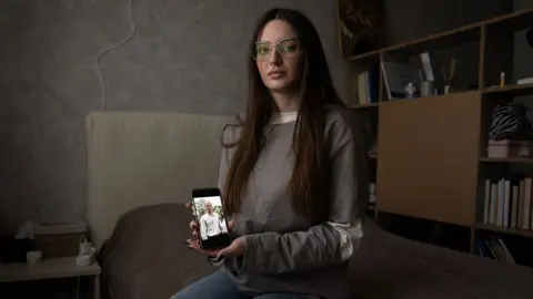 Julia Hripun sitting in her bedroom with a picture of her captive father on her iPhone