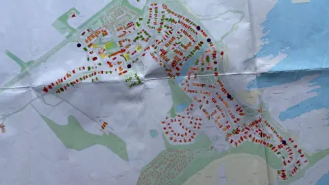 A paper map of Beadnell which shows houses coloured in different colours to denote whether they are lived in all the time or not. The orange to show holidays dominates the map.