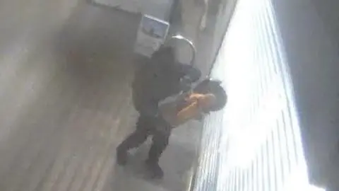 A man holding what appears to be an angle grinder outside a shop on CCTV footage