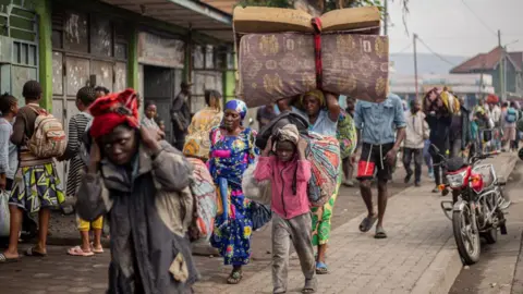 Residents carry their belongings as they flee from Kibati, where fighting has intensified, towards the city of Goma on January 26, 2025.