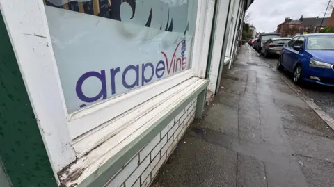 A window of the Grapevine building, at an angle, is prominent in the photo on the left. Cars are parked on the street on the right of the image.