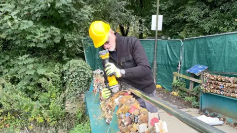 Mike Hall using a power tool to cut a wire on Weir Bridge in Bakewell and remove the padlocks