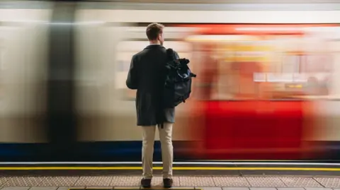 Business man carrying large backpack waits to get on the tube in London