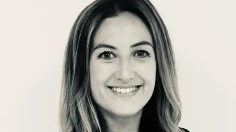 Hannah Ogden Hannah, a woman with long hair, smiles for the camera. The image is black and white.