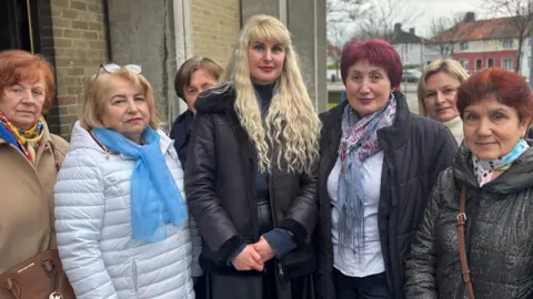 A group of Ukrainian women standing outside of a church wearing winter coats smile at the camera