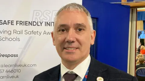 BBC/Martin Heath Simon Frazer with short hair wearing a black jacket and tie