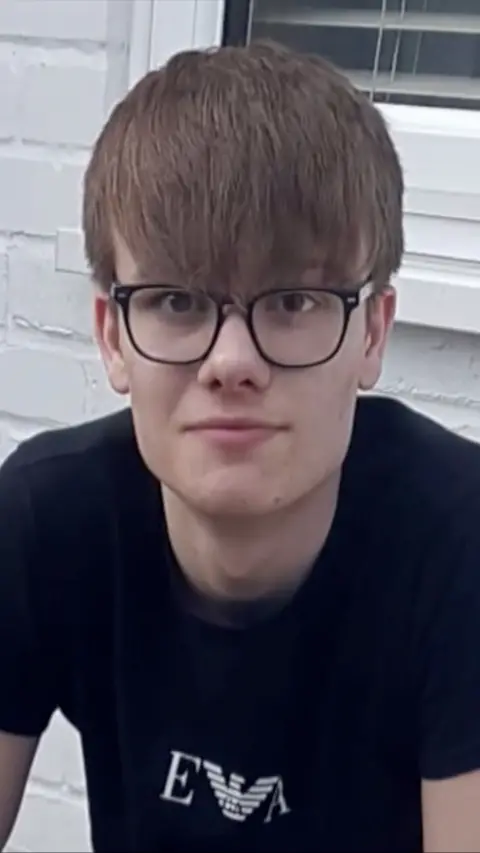 Teenager with dark hair and glasses wearing black t-shirt 