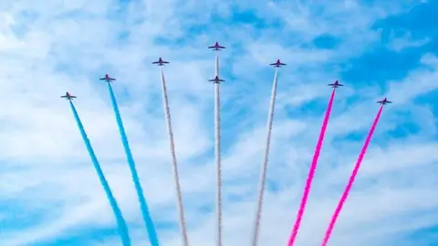 Claire Hartley Several planes fly in formation, leaving colorful vapour trails behind them