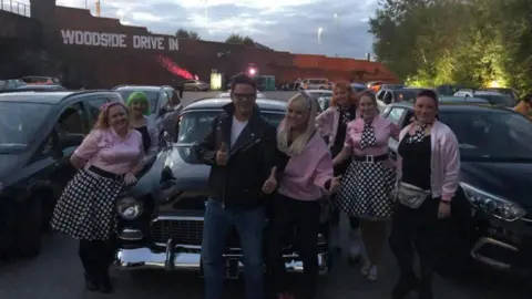 Karen Hall/Facebook A group of people stand in Grease-themed outfits at the drive-in. 