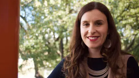 ABC A woman with long dark hair and big earrings smiles at the camera.