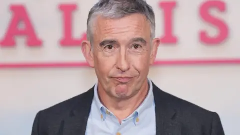 PA Steve Coogan in a light shirt and dark suit jacket