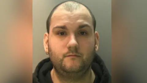 National Crime Agency A balding man, with one earring, wearing a black hoodie.