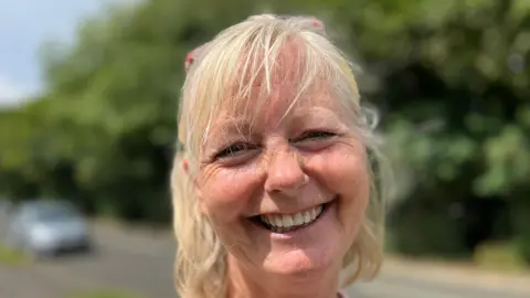 Blonde-haired Alison Cann smiles for the camera with a blurred out road behind her